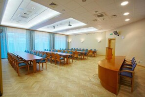 Un salón de conferencias con una larga mesa y sillas, un atril y un amplio ventanal con cortinas.