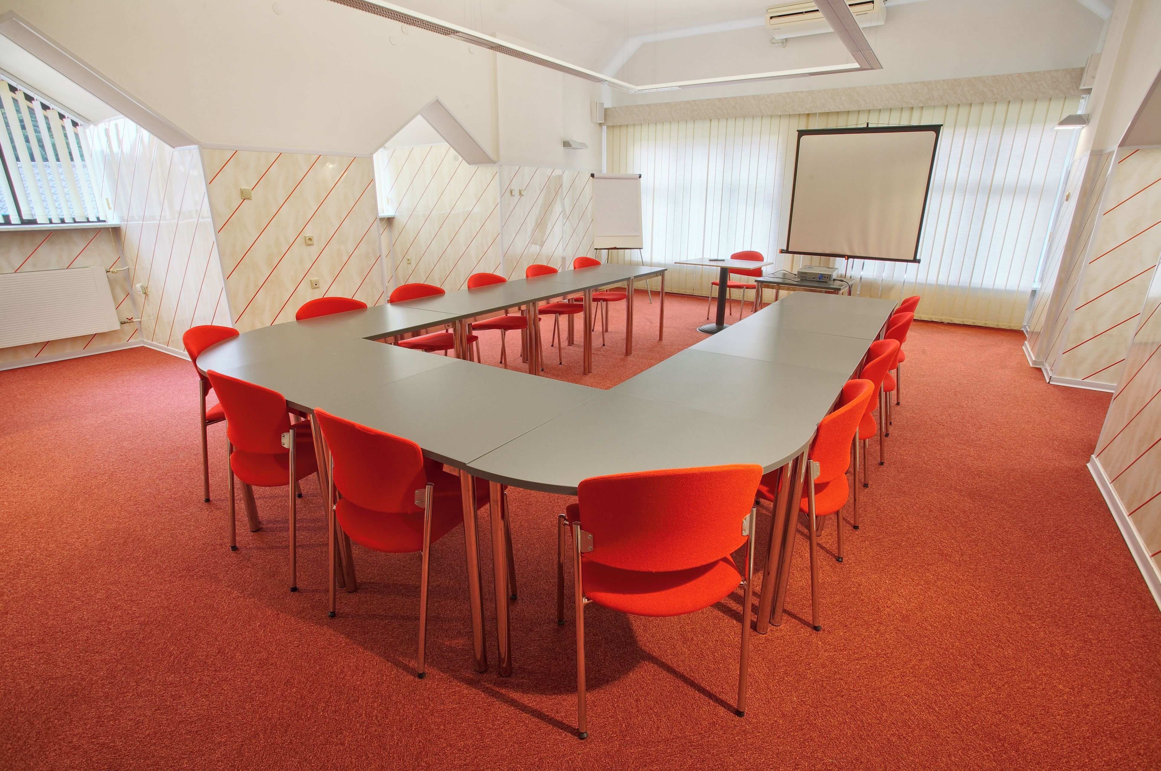 Un salón de conferencias con una larga mesa, sillas rojas, una pizarra y una pantalla para proyector.
