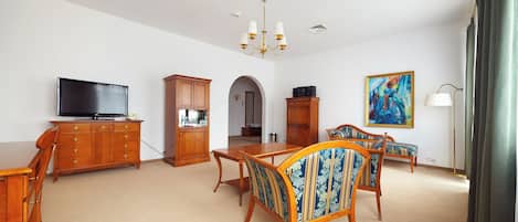 A spacious living room with a television, wooden furniture, a chandelier, and a painting.