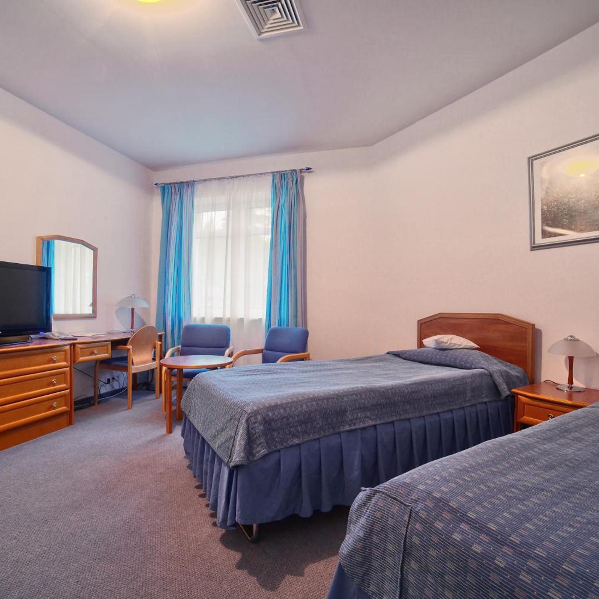 Habitación de hotel con cama, escritorio con computadora, silla, televisor y ventana con cortinas.