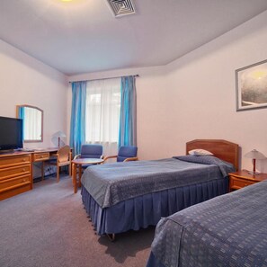Une chambre d’hôtel avec un lit, un bureau avec un ordinateur, une chaise, une télévision et une fenêtre avec des rideaux.