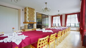 Comedor con mesas largas cubiertas con manteles rojos, sillas de madera y una lámpara de araña.