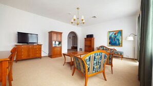 Un salón amplio con televisor, muebles de madera, una araña y un cuadro en la pared.