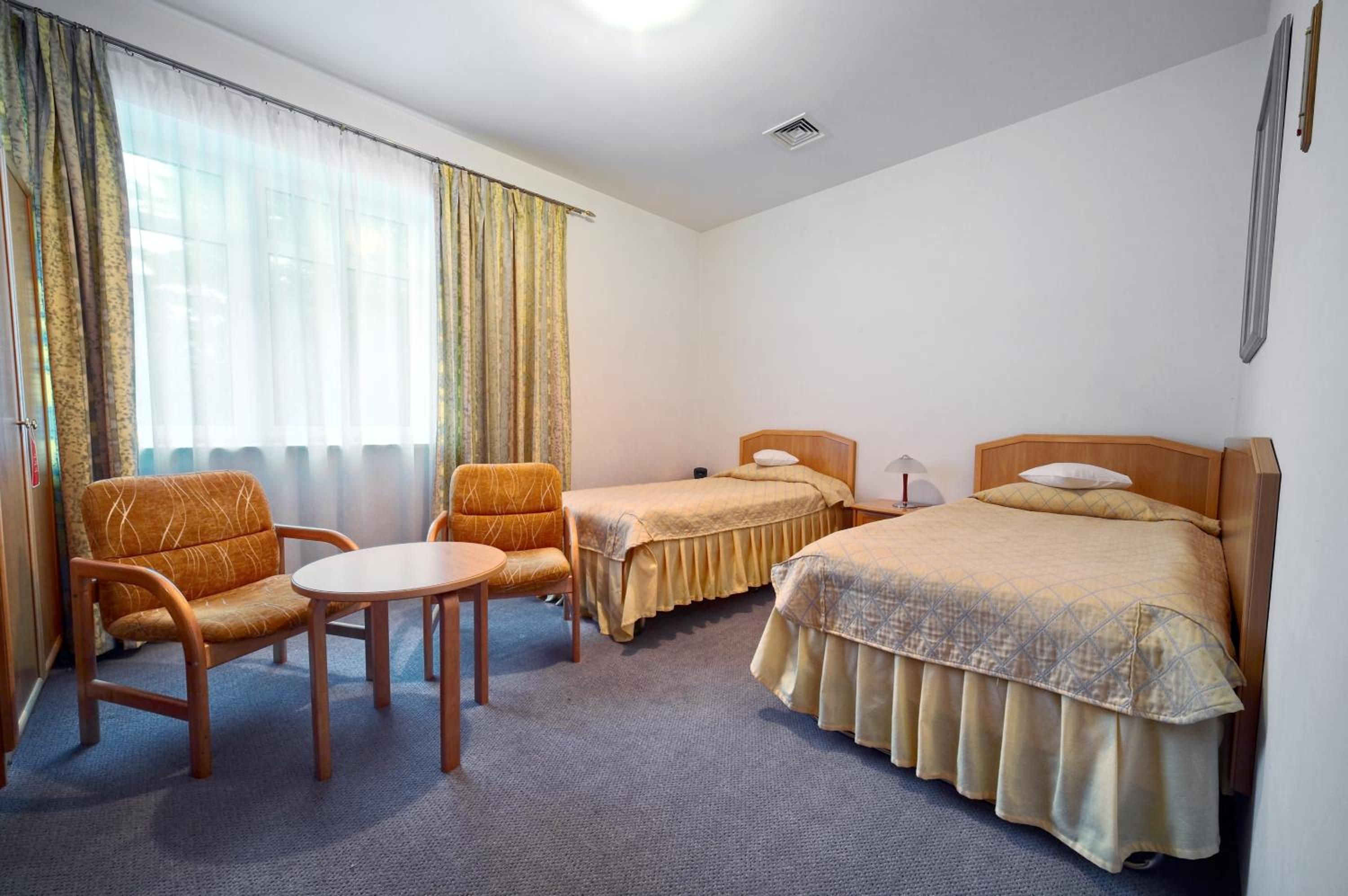 A hotel room with two single beds, a sofa, a small table, and a chair.
