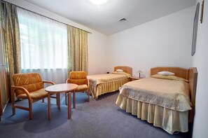 Habitación de hotel con dos camas individuales, un sofá, una mesita y una silla.