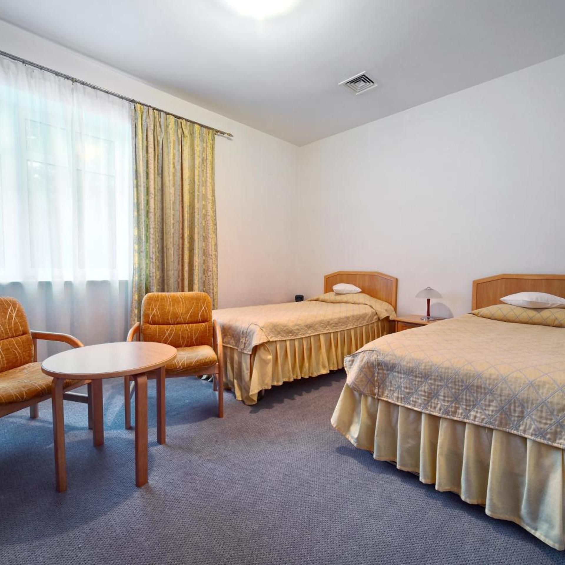 A hotel room with two beds, a chair, a small table, and a window with curtains.