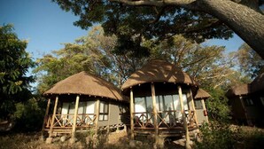 Two thatched-roof huts with wooden railings, surrounded by trees and vegetation. - Jambo Impala Ecolodge (Kisumu)