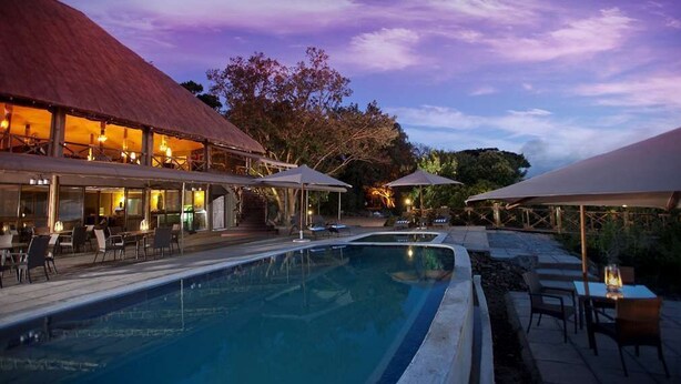 A pool area with outdoor seating and umbrellas, surrounded by buildings with a red roof. - Jambo Impala Ecolodge (Kisumu)