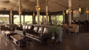 A spacious indoor area with a large leather sofa, wooden tables, and hanging pendant lights. - Jambo Impala Ecolodge (Kisumu)