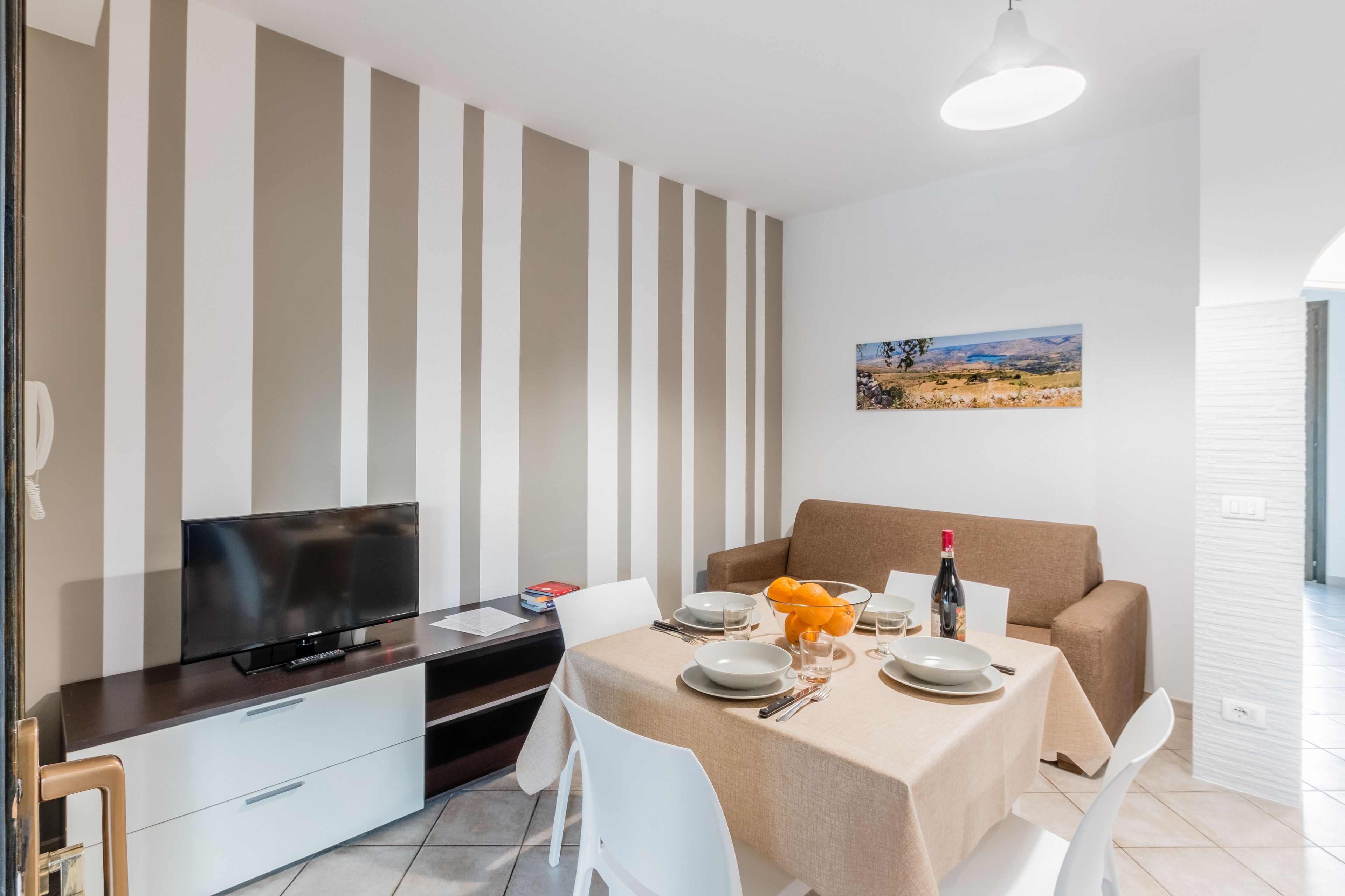 A modern dining area with a table set for two, a sofa, and a TV on a dark wooden console.