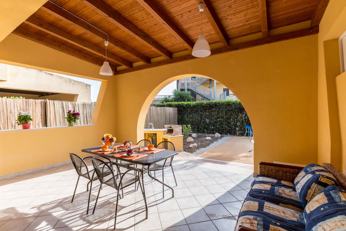 An outdoor patio with a dining table and chairs, a sofa, and a wooden ceiling.