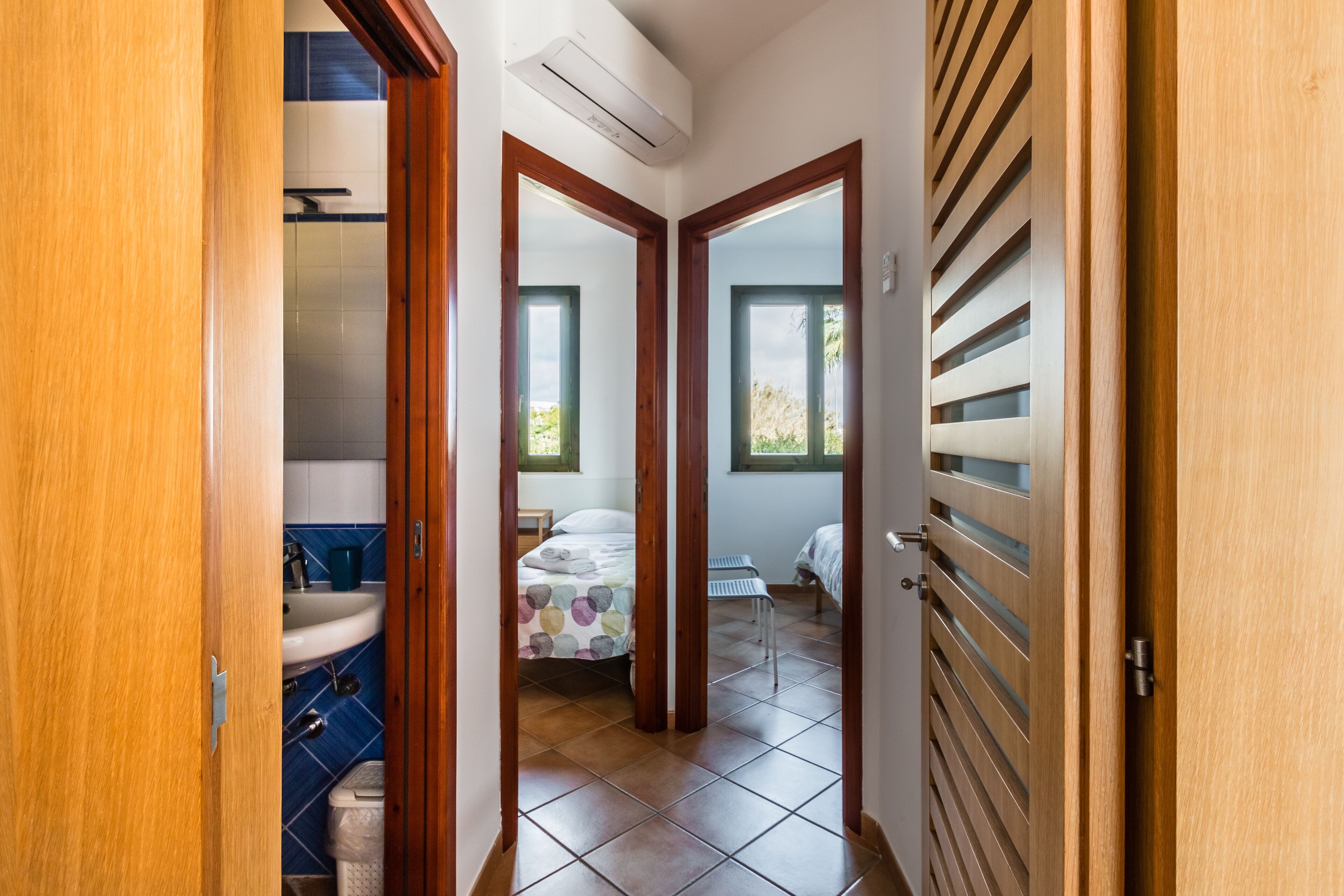 Un pasillo que conduce a un dormitorio con cama, ventana y baño con lavabo y ducha.