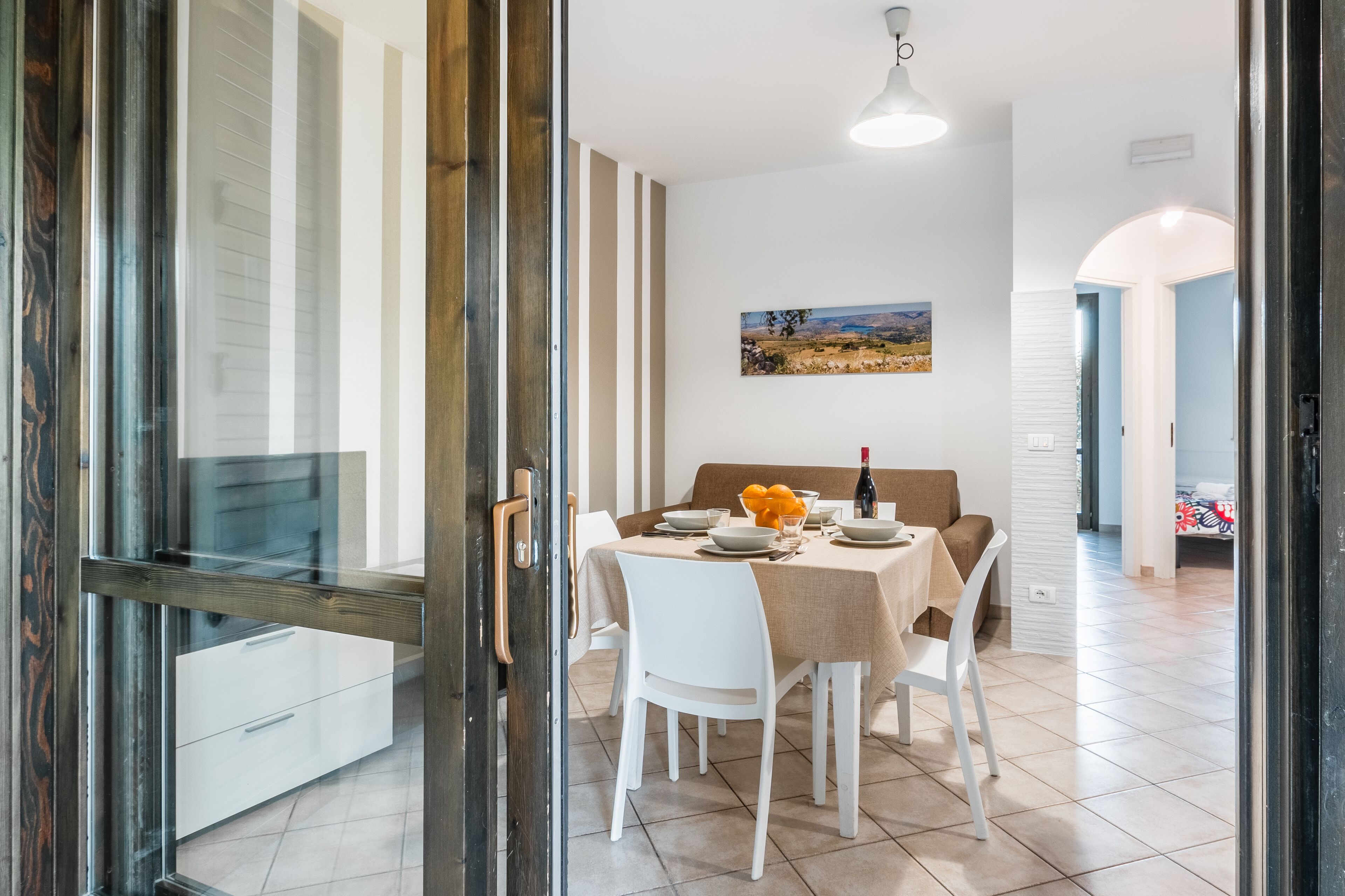 Un comedor con una mesa lista para dos personas, un cuadro en la pared y vistas a través de un ventanal.