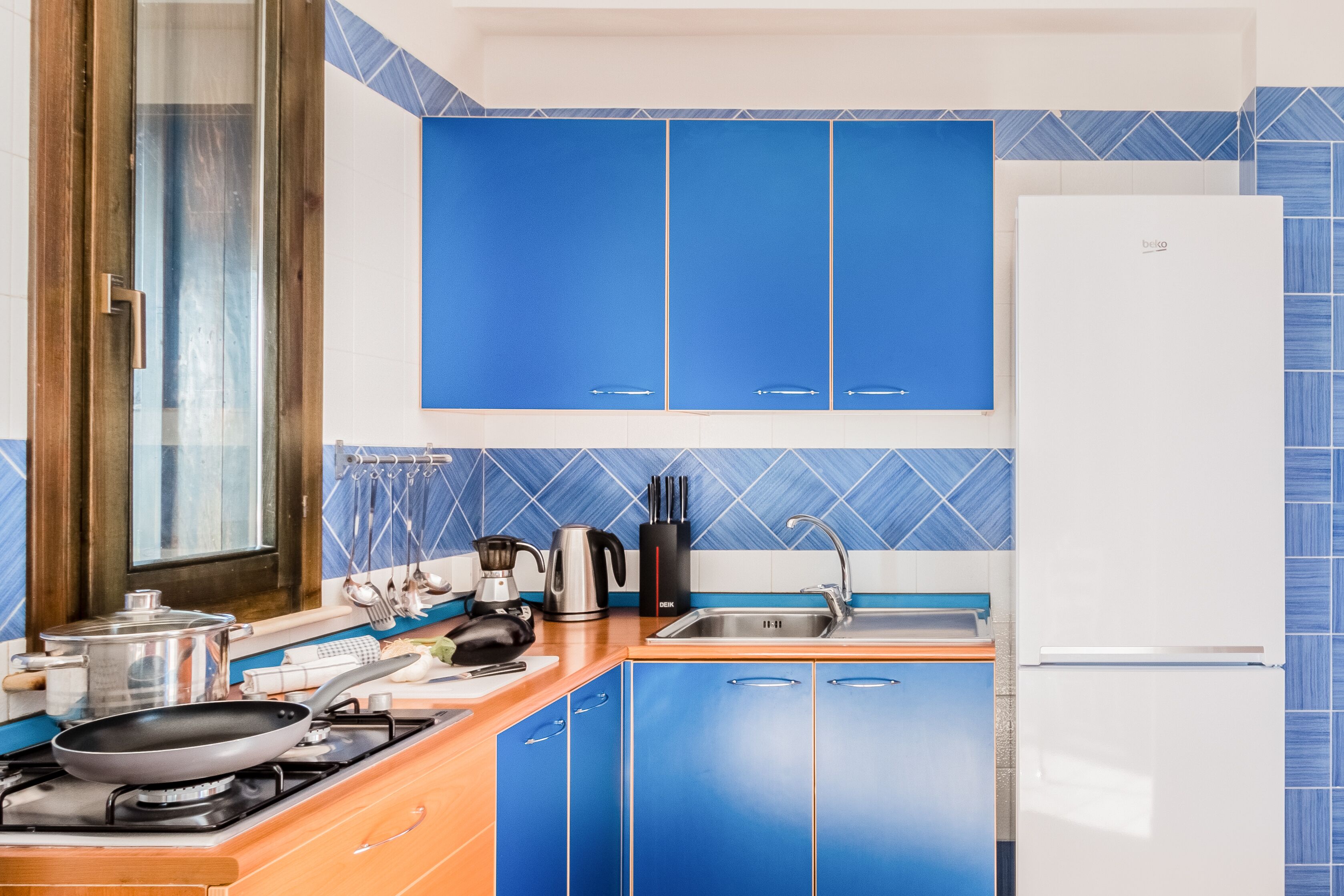 A kitchen with blue cabinets, a stove, a sink, and a refrigerator.