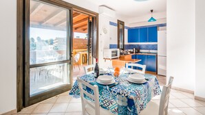 A dining area with a table set for two, a kitchen in the background, and a large window with a view of the outside. - Residence Andrea Doria (Ragusa)