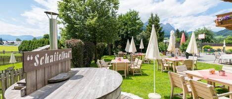 Un espace extérieur aménagé avec des tables et des chaises en bois, entouré de verdure et agrémenté d’une pancarte indiquant « Schattenbad ».
