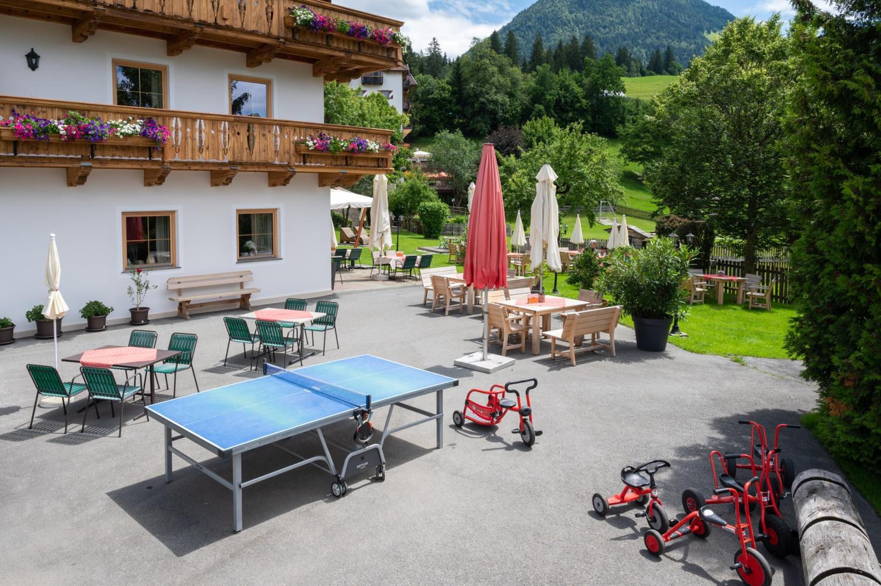 An outdoor patio with tables and chairs, a ping pong table, and children's tricycles.