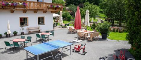 An outdoor patio with tables and chairs, a ping pong table, and children's tricycles.