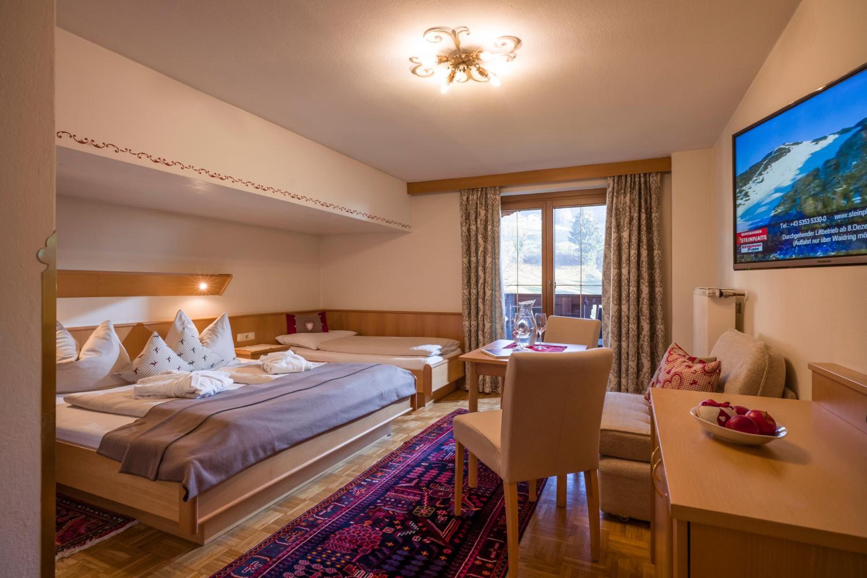 Ein Hotelzimmer mit Bett, Schreibtisch, Stuhl, kleinem Tisch, Fernseher und einem Fenster mit Vorhängen.
