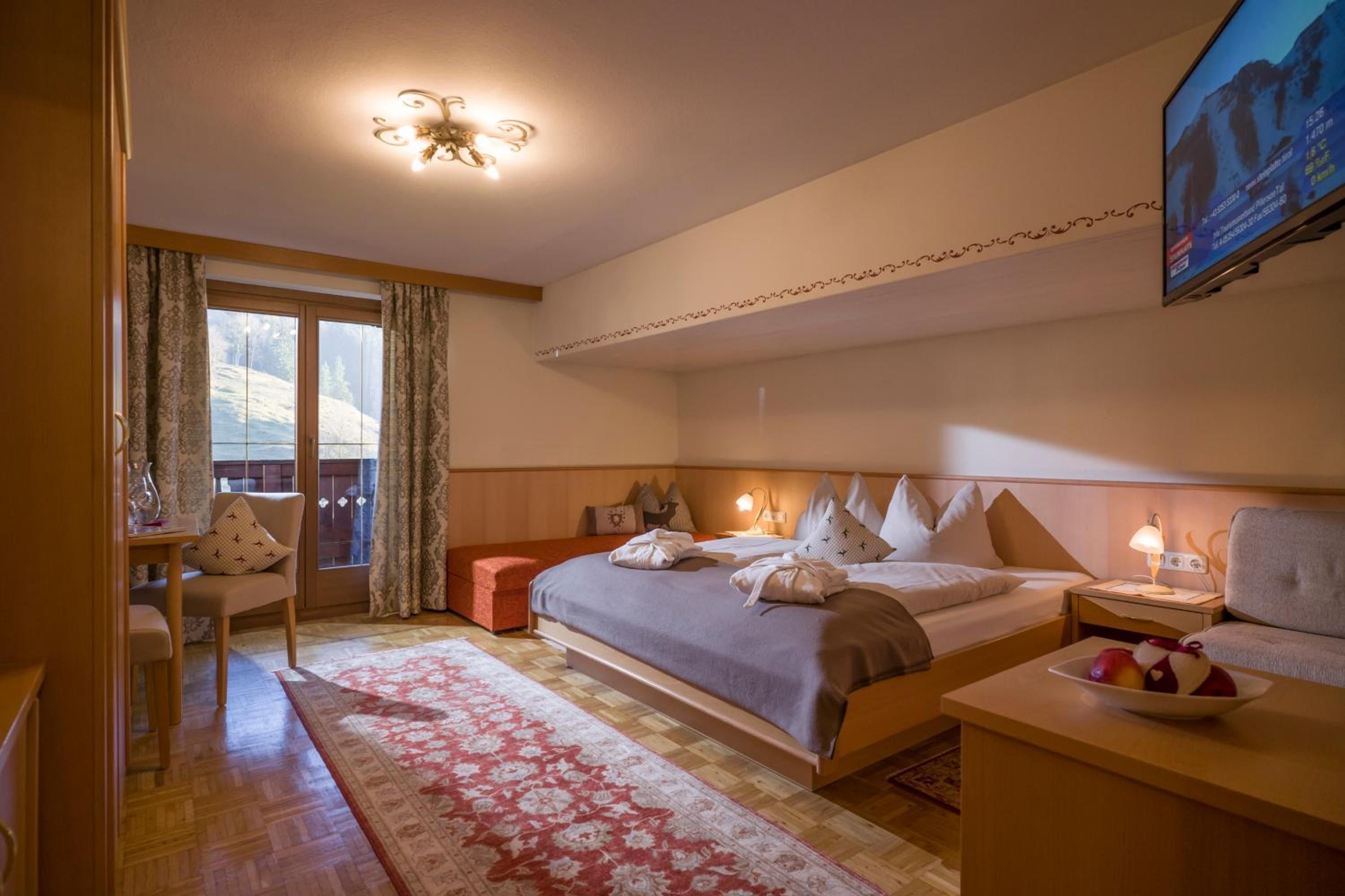 A hotel room with a bed, bedside table, chair, and a television mounted on the wall.