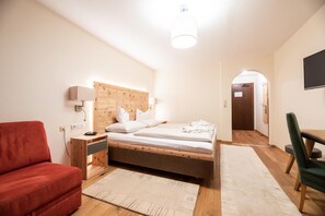 A hotel room with a wooden headboard, two beds, a red chair, a desk, and a TV.