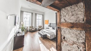 Quarto de hotel moderno com teto de madeira, uma cama grande, escrivaninha e um espaço de estar com cadeiras.