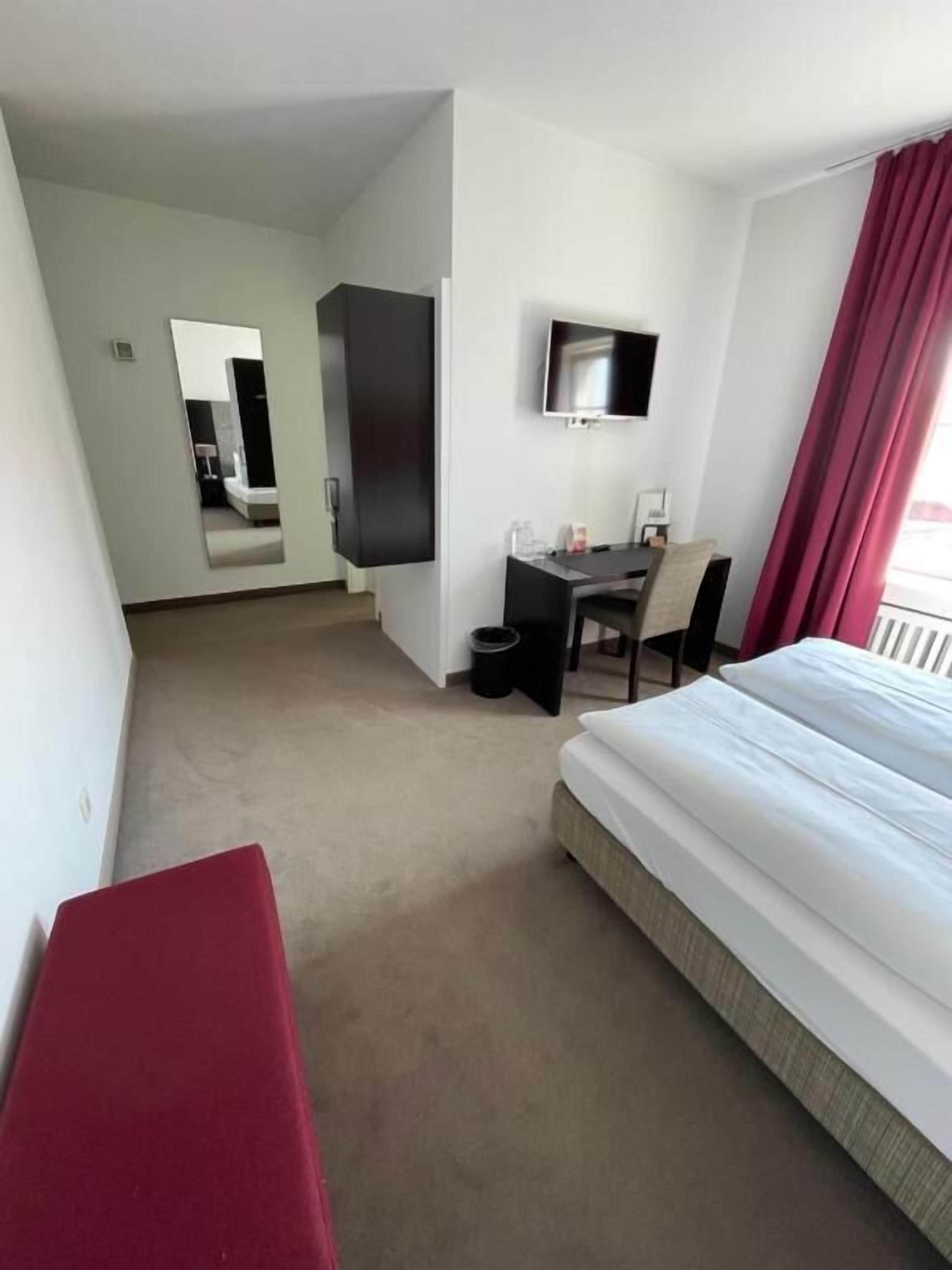 A hotel room with a bed, a desk, a chair, a TV, and a mirror.