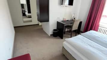 A hotel room with a bed, a desk, a chair, a TV, and a mirror.