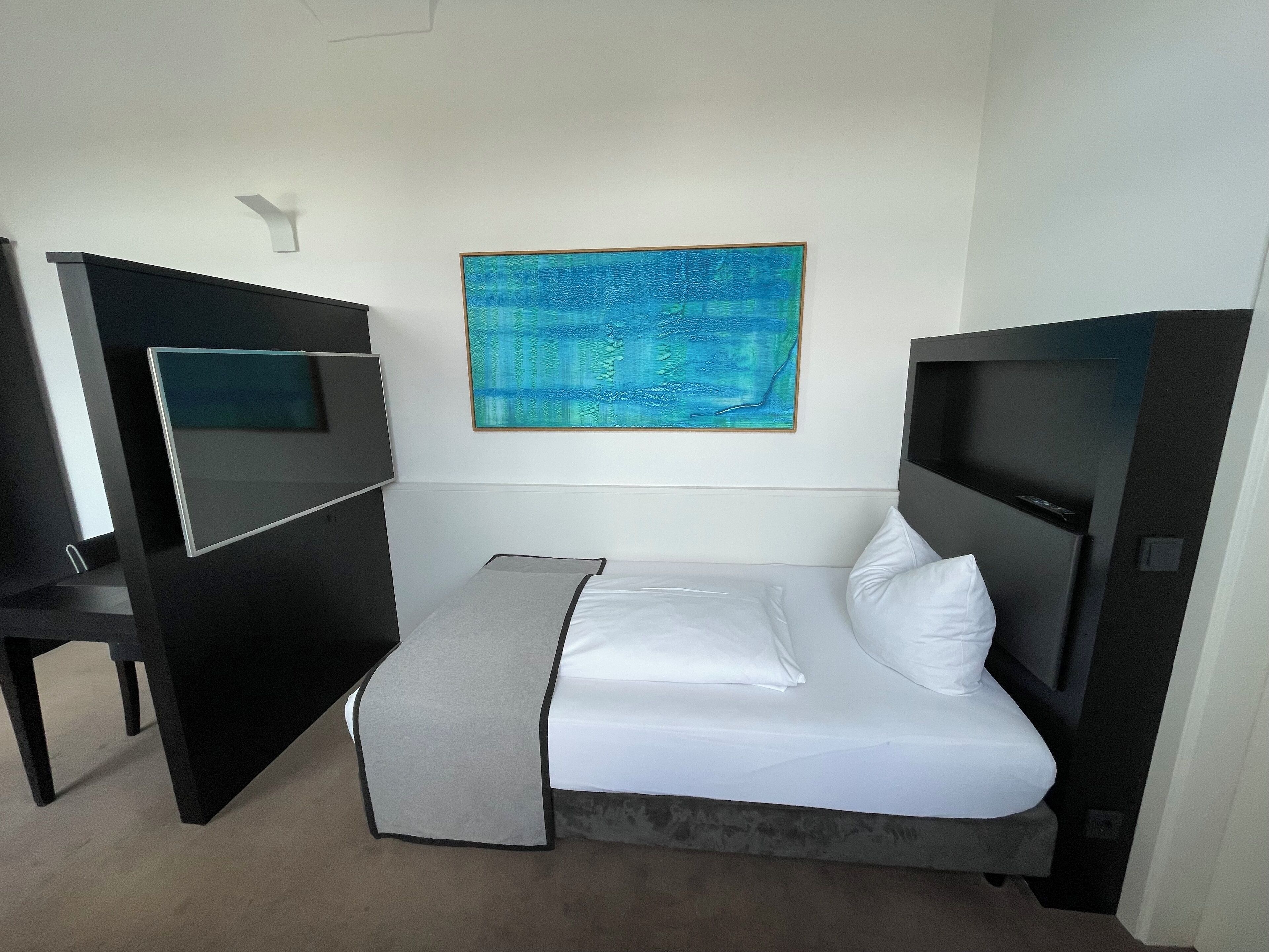 A hotel room with a bed, a desk, and a large abstract painting on the wall.