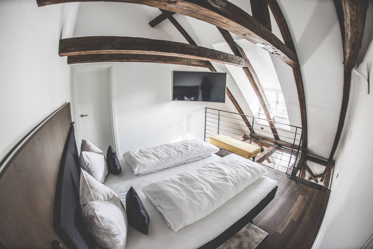 A bedroom with a loft bed, a small desk, and a television mounted on the wall.