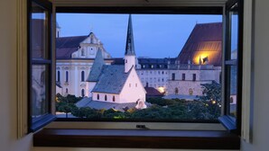 Vista da janela com vista para um conjunto histórico de edifícios, incluindo uma torre de igreja imponente e construções adjacentes.