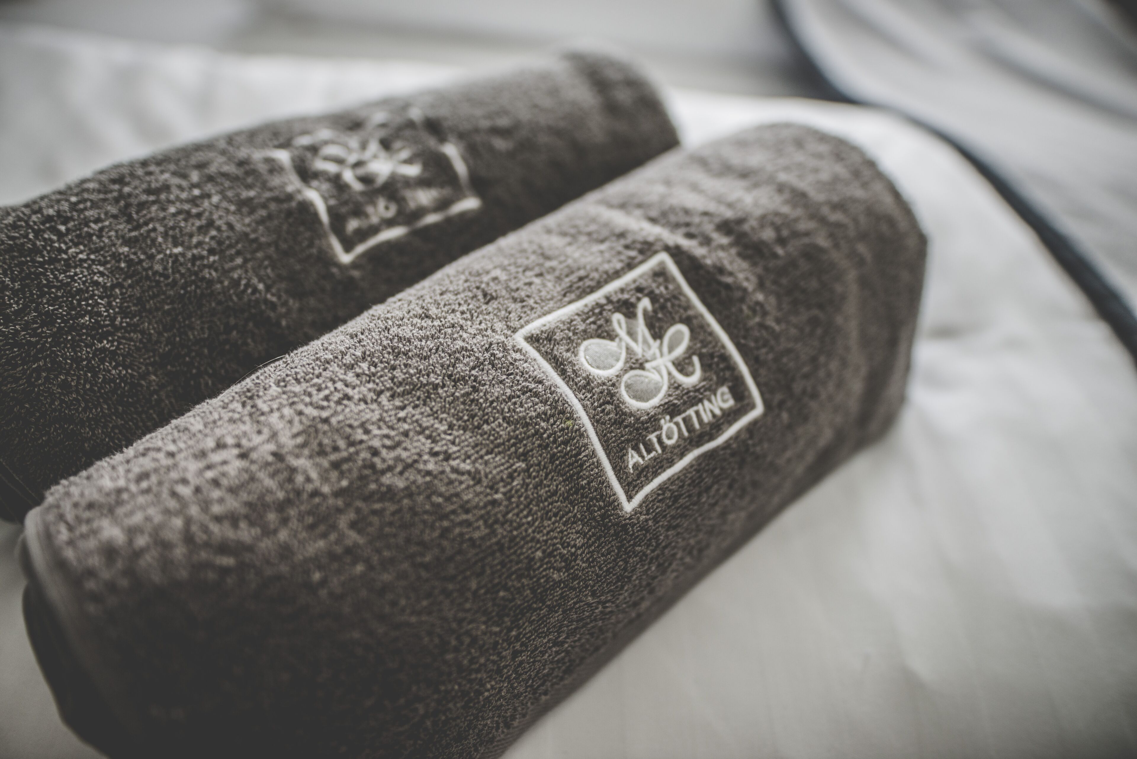 Gerollte Handtücher mit aufgestickten Logos auf einem Bett.