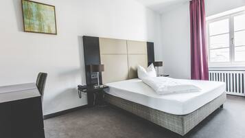 Ein Hotelzimmer mit Bett, Nachttischlampen, einem Schreibtisch und einem Fenster mit Vorhängen.