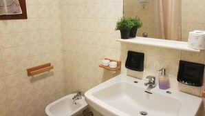 A bathroom with a bidet, a sink, a mirror, a towel rack, a shelf with toiletries, and a potted plant. - B&B Magica Venezia (Mestre)