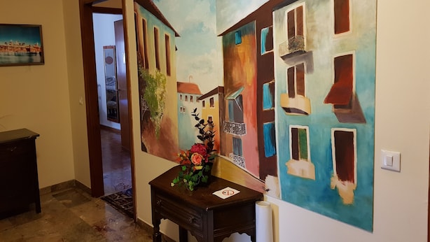A hallway with a large abstract painting of buildings and a small table with a vase of flowers. - B&B Magica Venezia (Mestre)