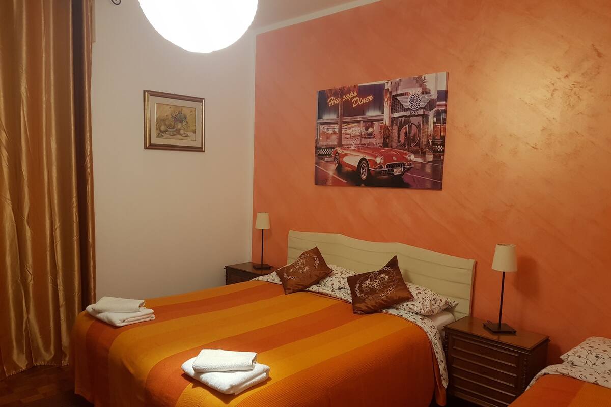 A hotel room with two beds, orange bedding, a framed picture on the wall, and a lamp on each bedside table.