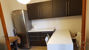 A compact kitchen with dark cabinets, a stainless steel refrigerator, a white countertop, and a small dining area with a chair. - B&B Magica Venezia (Mestre)