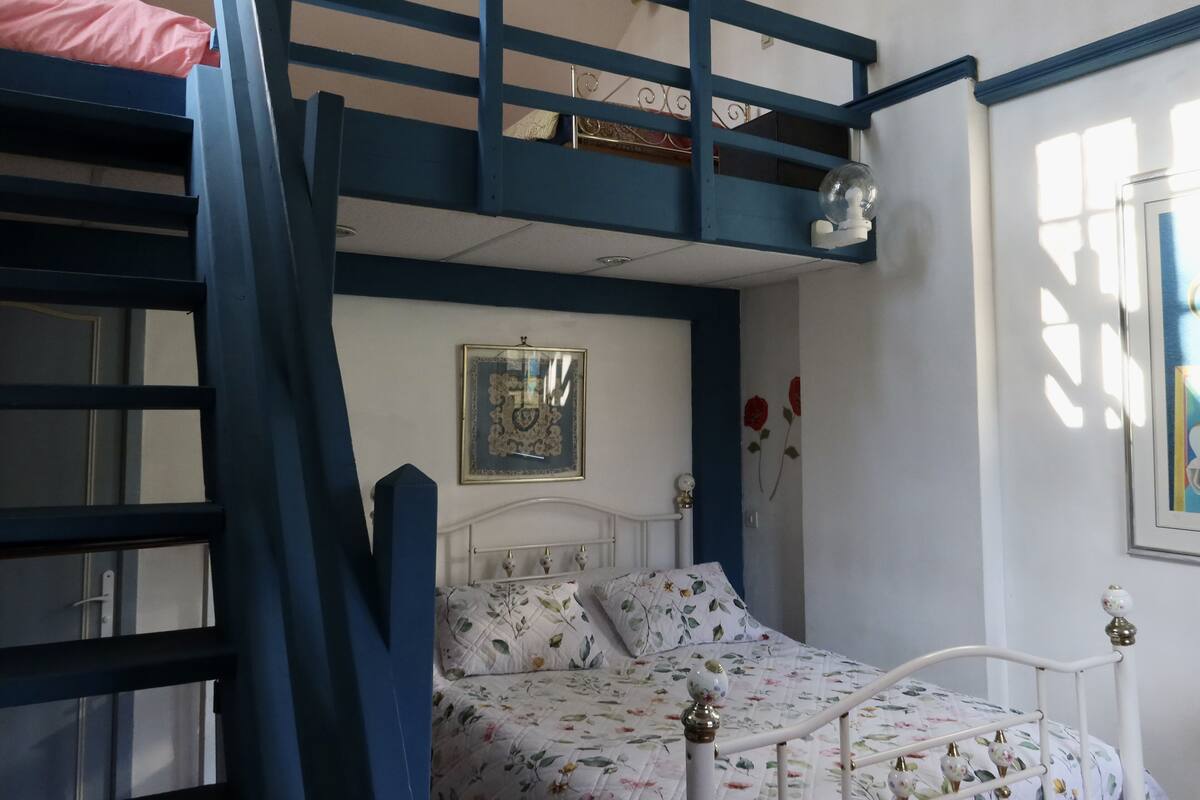 A bunk bed with a pink top bunk, a white headboard, floral bedding, and a framed picture on the wall.