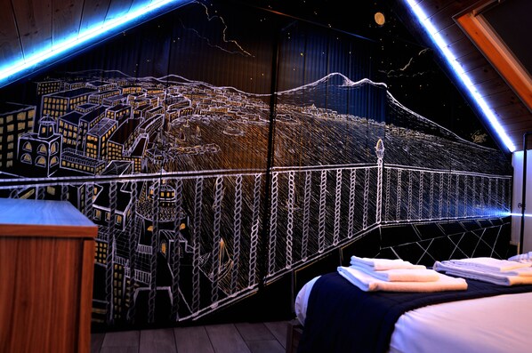 A bedroom with a mural of a cityscape, a bed with neatly folded towels, and a wooden headboard. - Palazzo Settembrini 49 (Naples)