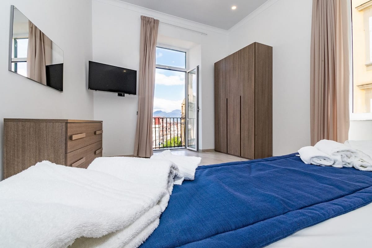 A modern hotel room with a bed, a TV, a wardrobe, and a balcony with a view.