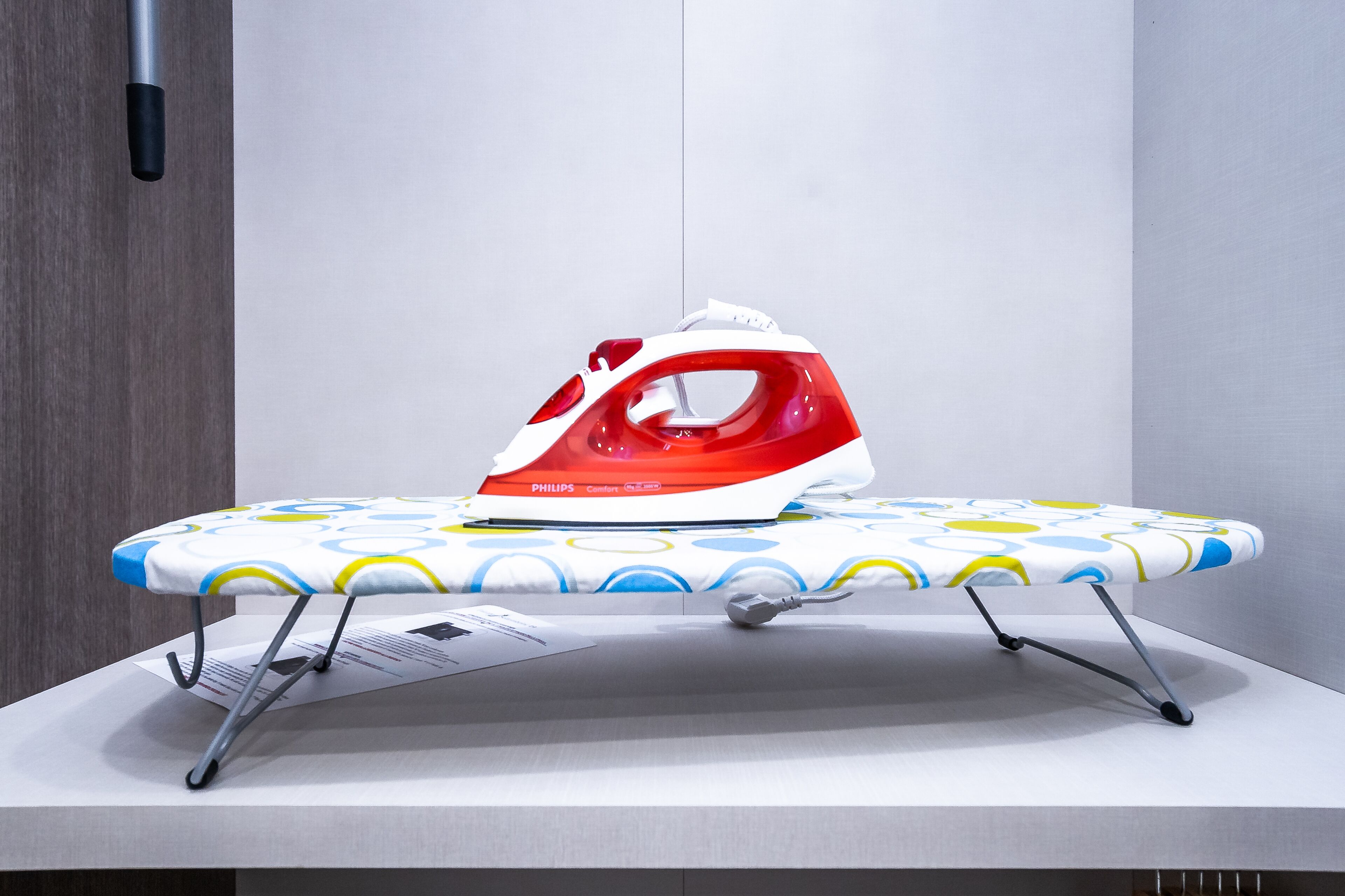 Une planche à repasser compacte recouverte d’un tissu à motifs, un fer à repasser et un support mural pour fer à repasser.