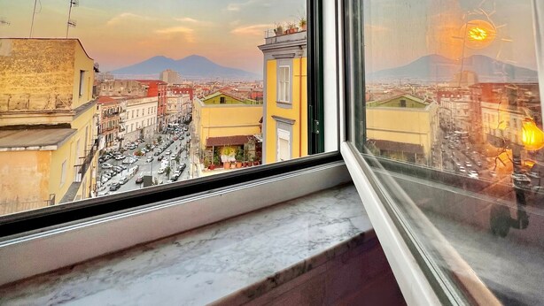 A view from a window overlooking a cityscape with buildings, a tower, and a mountain in the distance. - Palazzo Settembrini 49 (Naples)