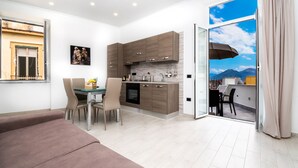 A modern kitchen with wooden cabinets, a dining area with a table and chairs, and a sliding glass door leading to a balcony with a mountain view. - Palazzo Settembrini 49 (Naples)