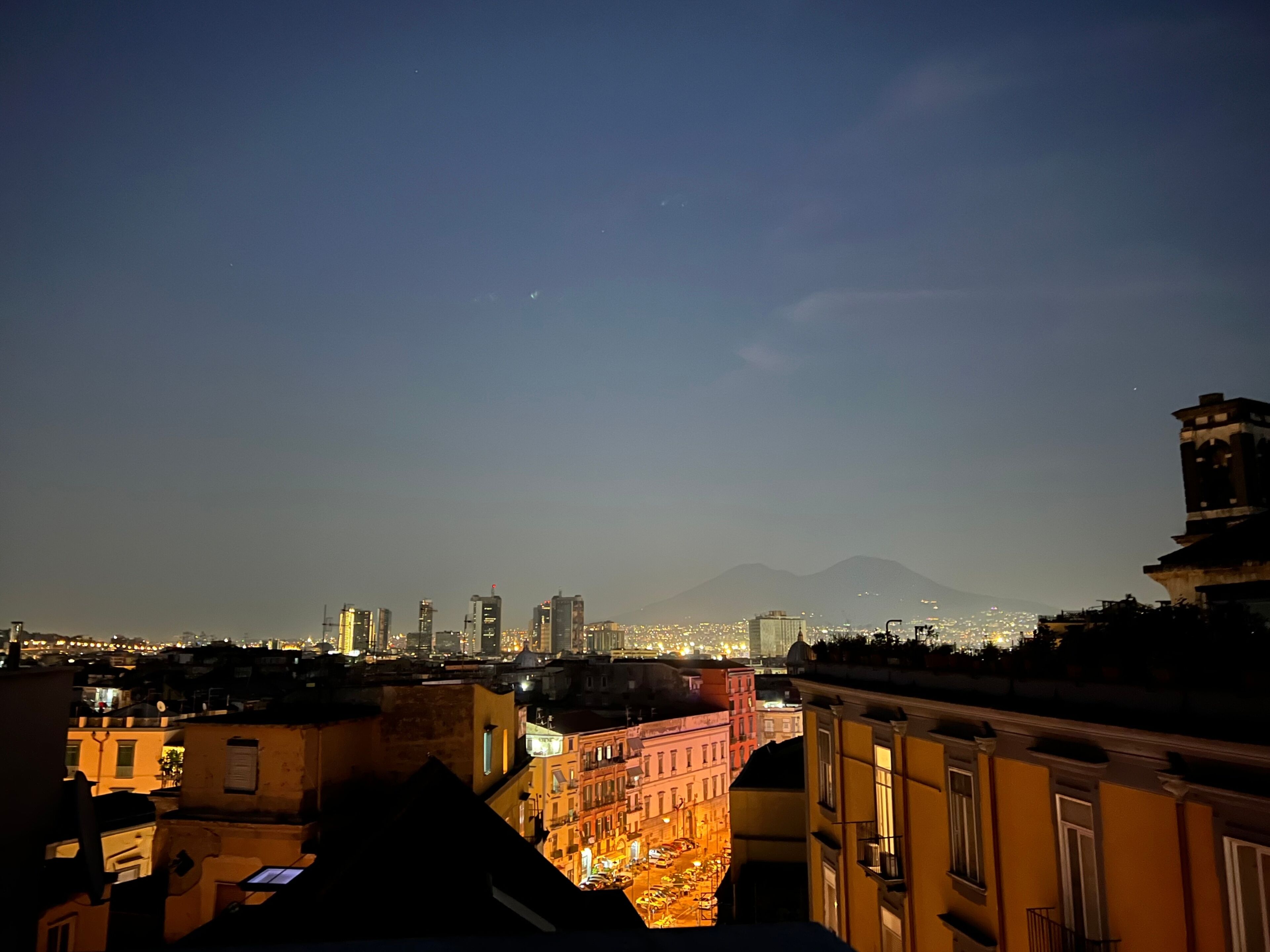 A nighttime cityscape with a view of a mountain in the distance and a densely packed urban area with illuminated buildings.