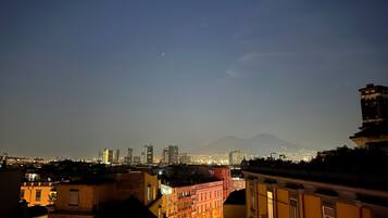 Une vue nocturne d’une ville, avec une montagne visible au loin et une zone urbaine densément peuplée, où les bâtiments sont illuminés.