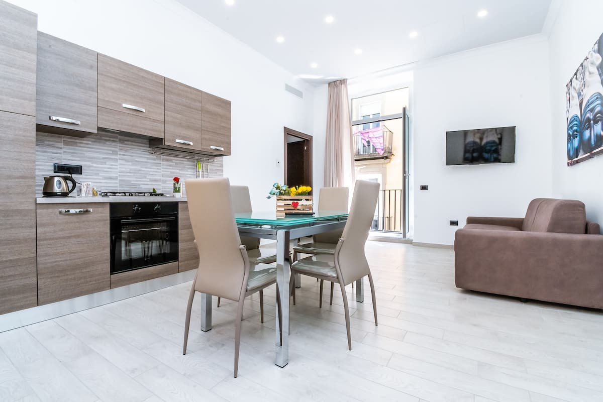 A modern kitchen with wooden cabinets, a dining table with chairs, and a living area with a sofa.