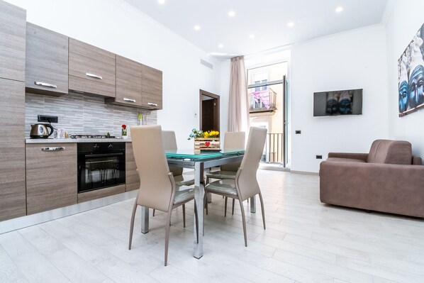 A modern kitchen with wooden cabinets, a dining table with chairs, and a living area with a sofa. - Palazzo Settembrini 49 (Naples)
