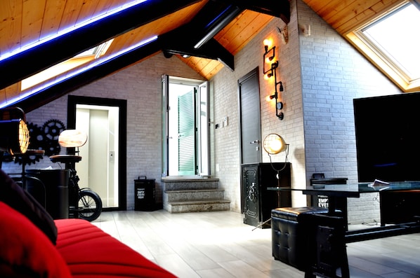 A loft-style room with a sloped ceiling, exposed wooden beams, a fireplace, a television, and a bicycle. - Palazzo Settembrini 49 (Naples)
