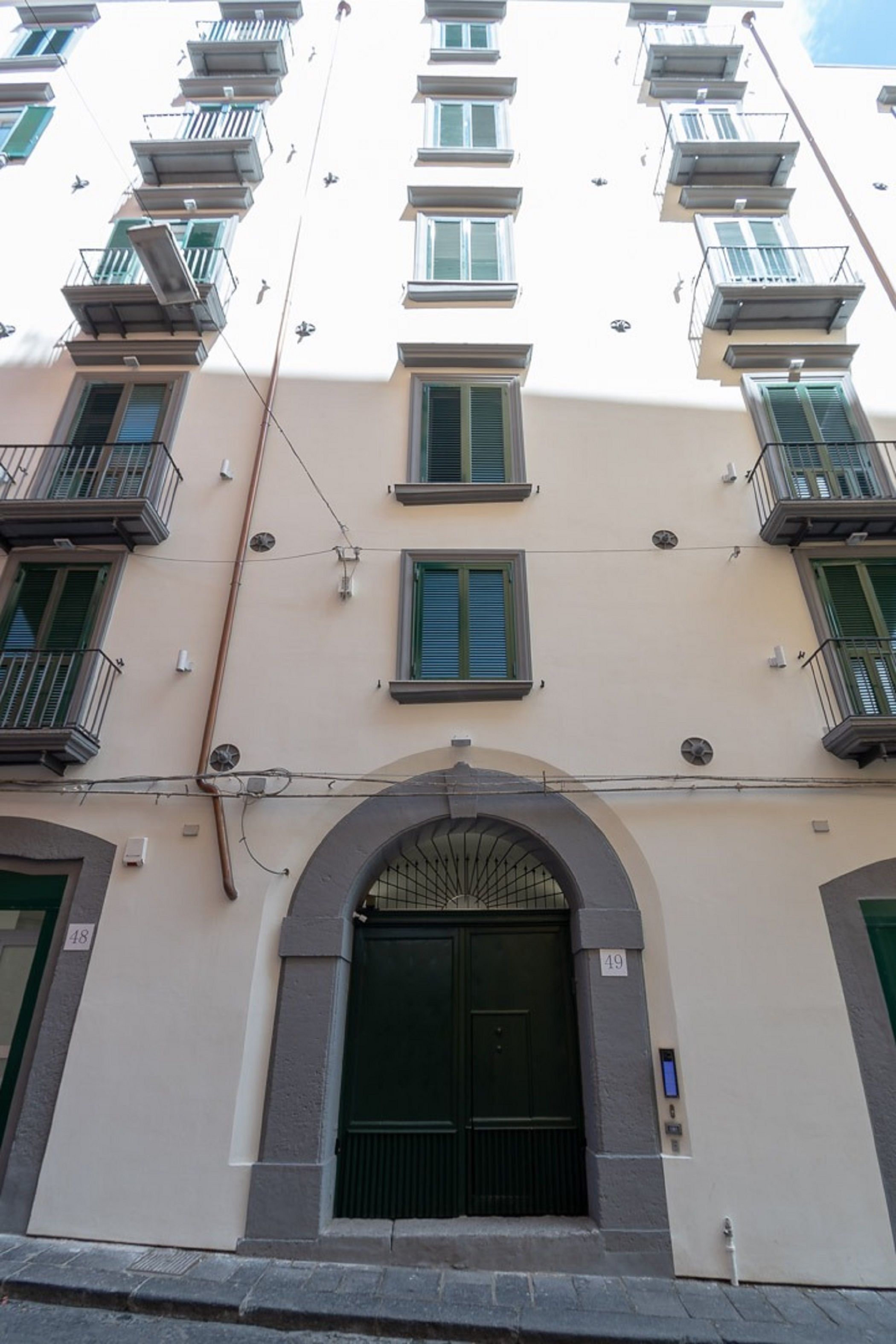 A multi-story building with balconies, a central entrance with a metal gate, and a series of windows with shutters.