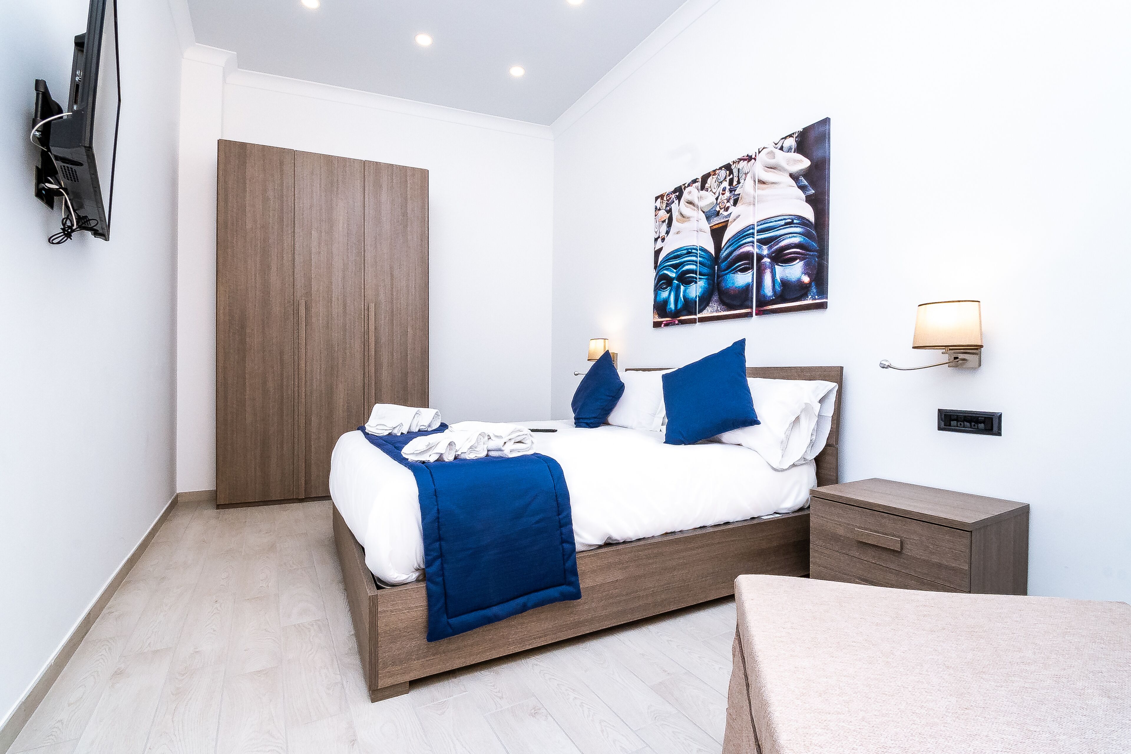 A modern bedroom with a bed, bedside tables, a wardrobe, and a wall-mounted TV.